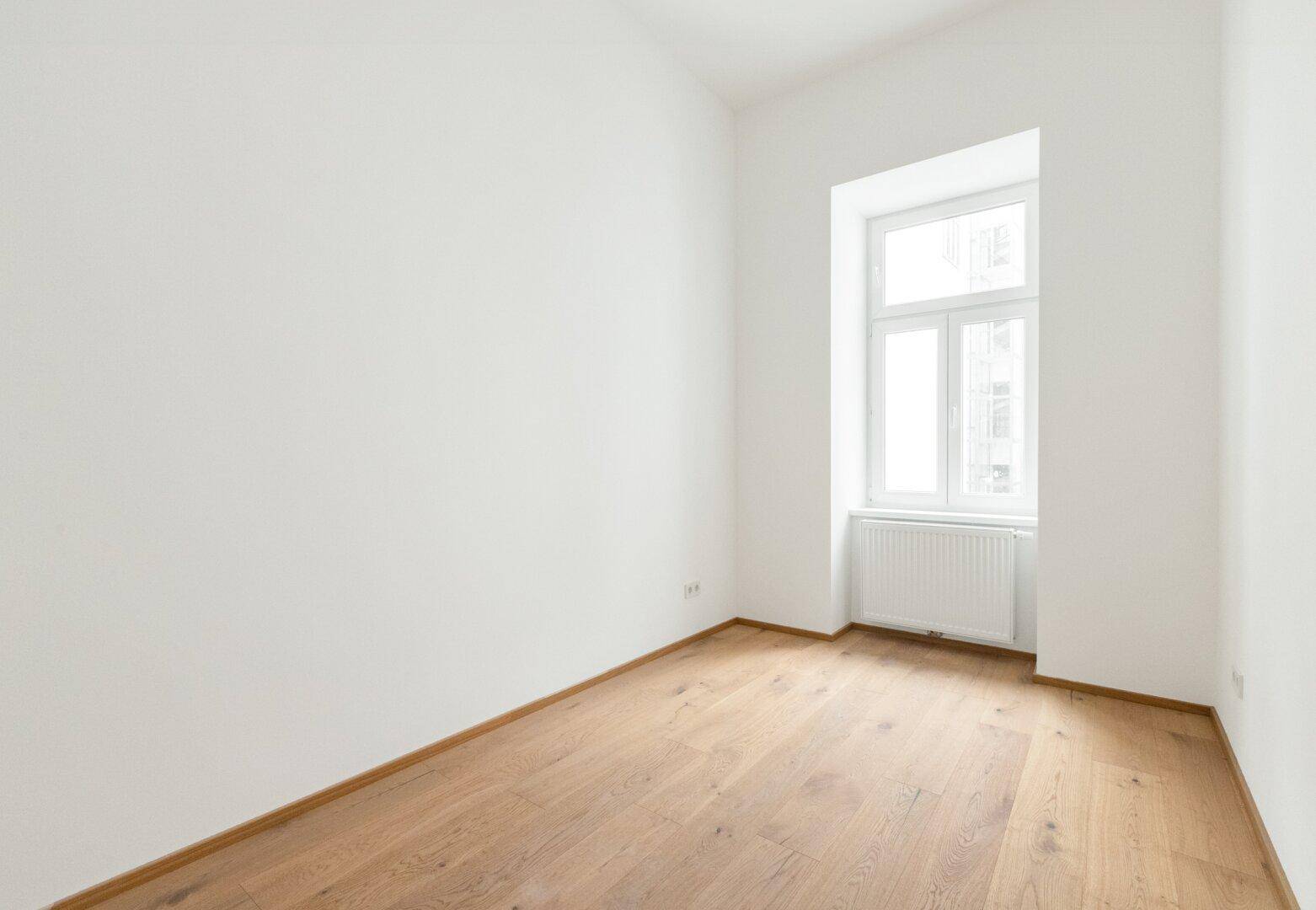 Heller, leerer Raum mit Holzboden und einem Fenster, ideal als Schlafzimmer.