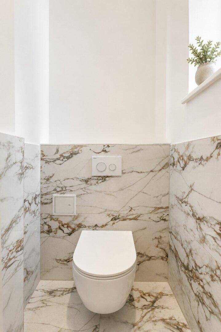 Separates WC mit eleganten Marmorfliesen und wandhängender Toilette.