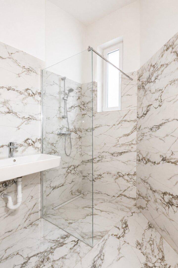 Modernes Badezimmer mit Marmorfliesen, begehbarer Dusche und Fenster.