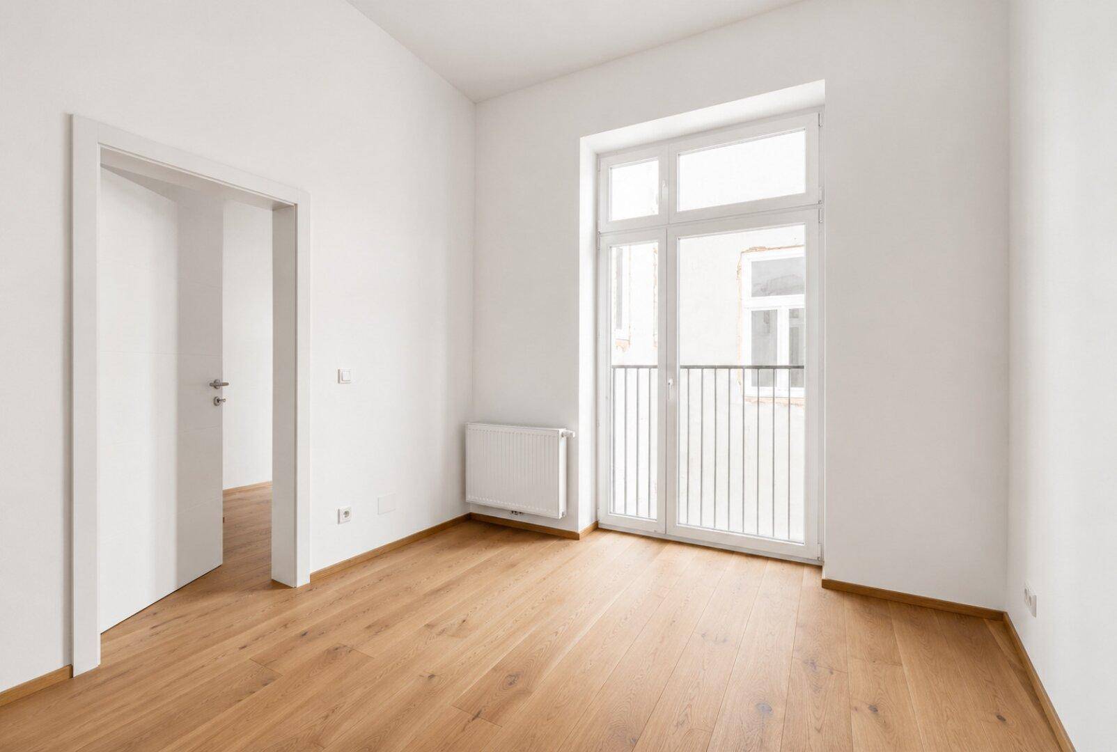 Helles, leeres Schlafzimmer mit Holzboden und einem französischen Balkon.