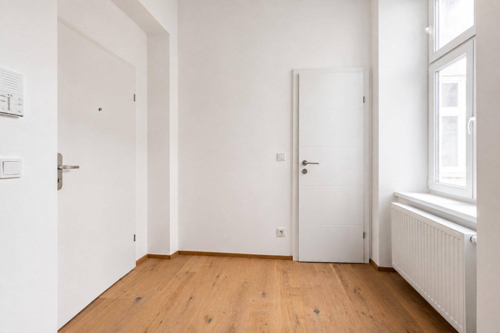 Heller Eingangsbereich mit Holzboden, weißen Wänden und einem Fenster.