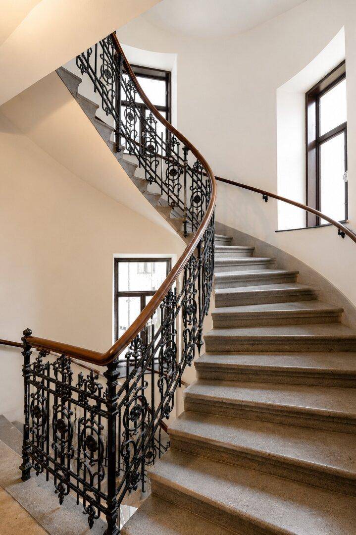 Elegantes Treppenhaus mit kunstvollem schmiedeeisernem Geländer und Holzhandlauf in einem historischen Gebäude.