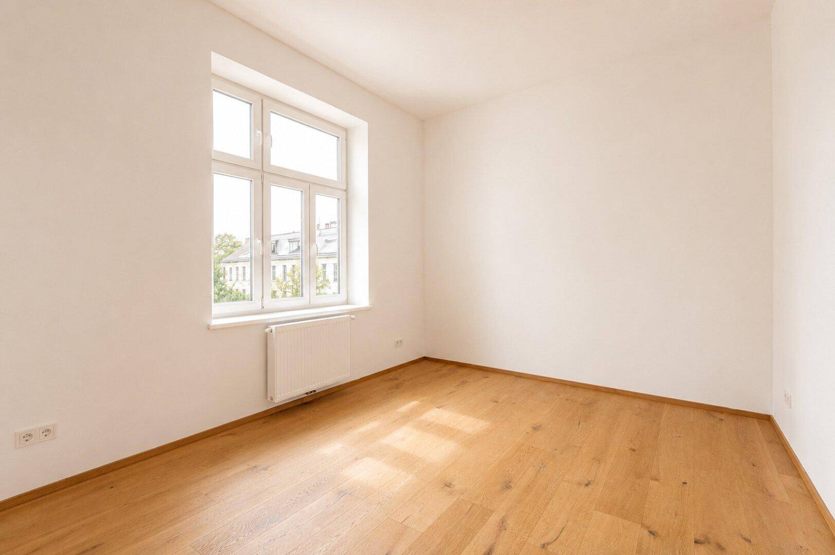 Unmöbliertes Schlafzimmer mit Holzboden und großem Fenster, bietet viel natürliches Licht.