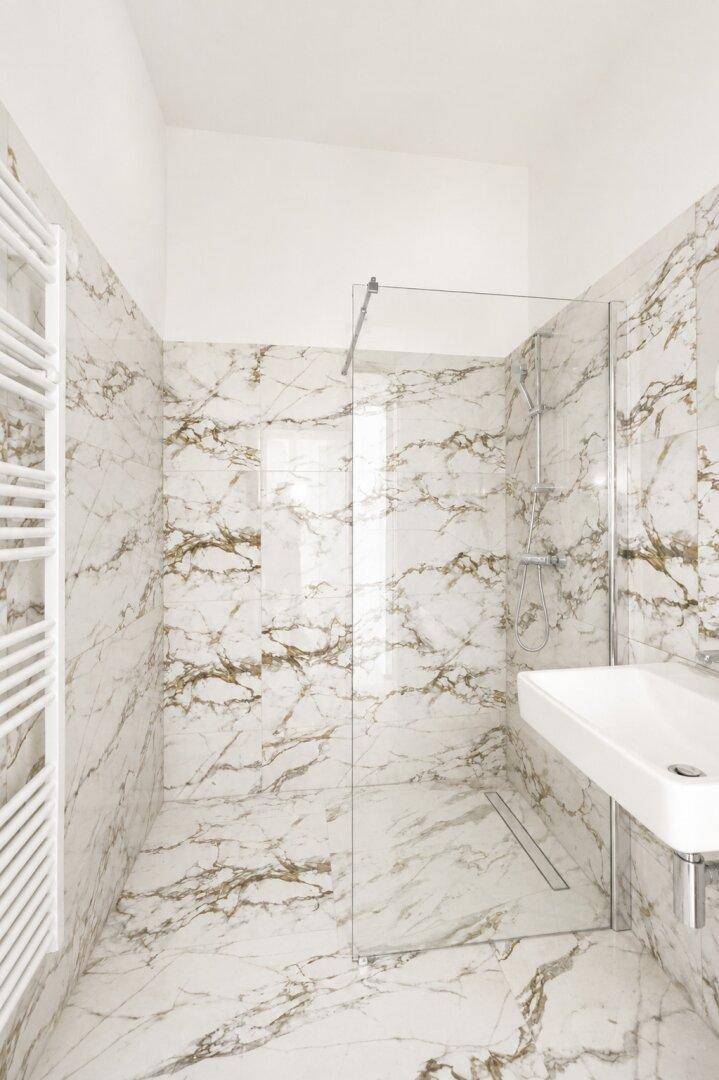 Modernes Badezimmer mit begehbarer Dusche und eleganten Marmorfliesen an Wänden und Boden.