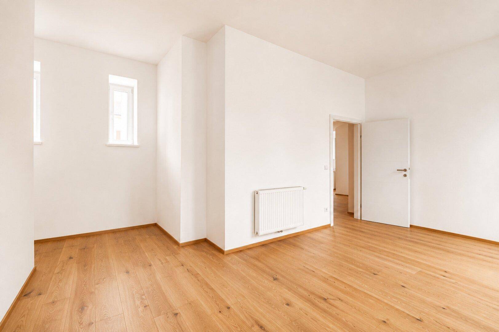 Heller, unmöblierter Raum mit Holzboden und zwei Fenstern, vielseitig nutzbar.