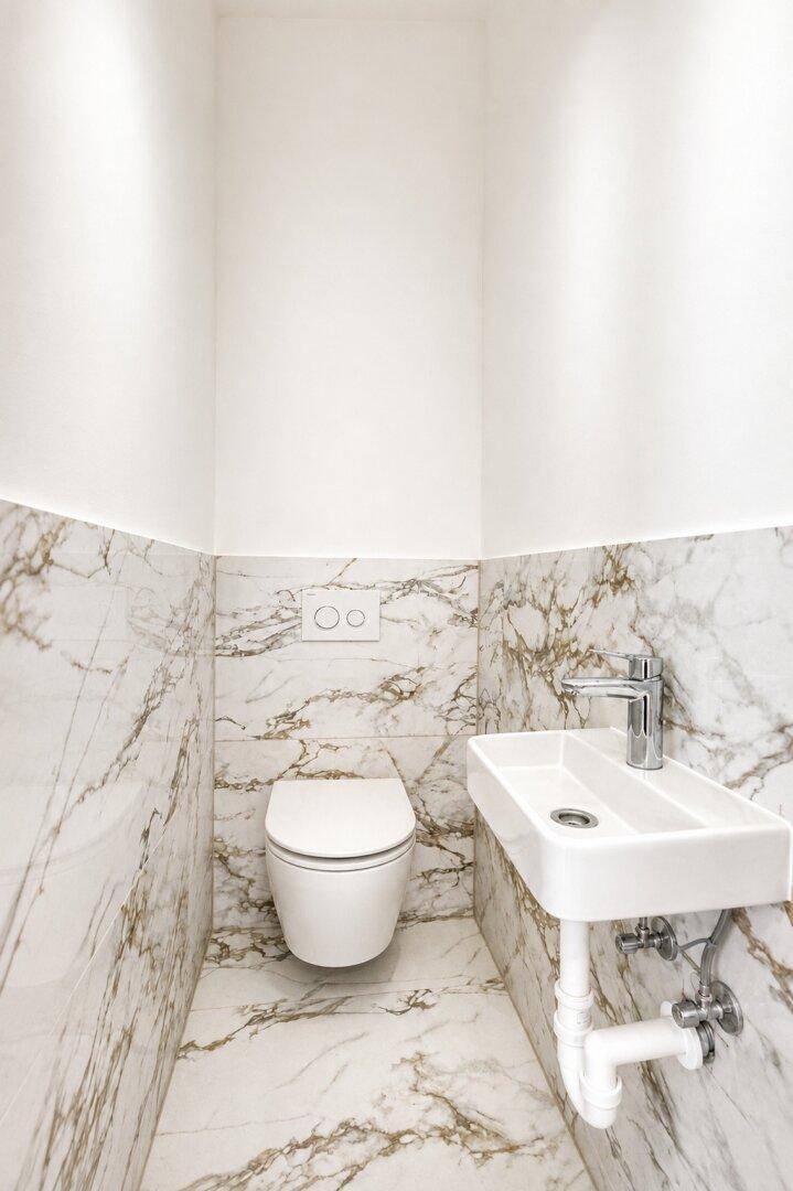 Separates Gäste-WC mit Wand-WC und kleinem Waschbecken, elegant gefliest.