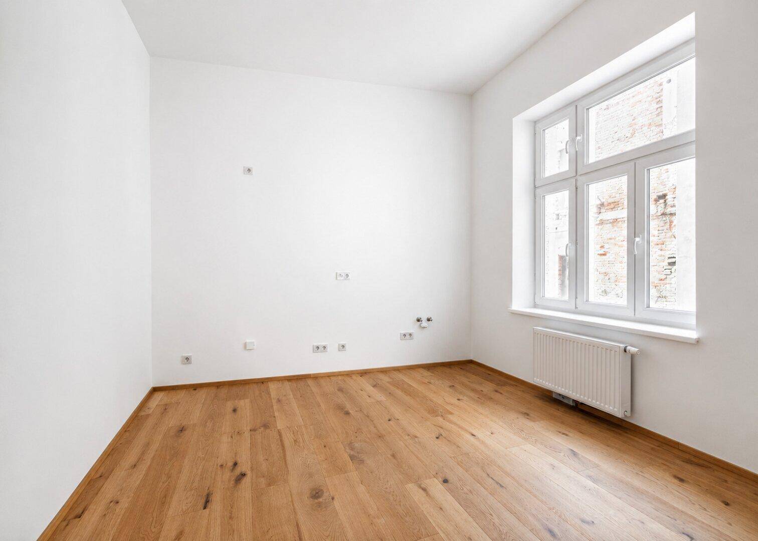 Unmöblierte Küche mit Holzboden und großem Fenster, bereit für die Installation einer Einbauküche.