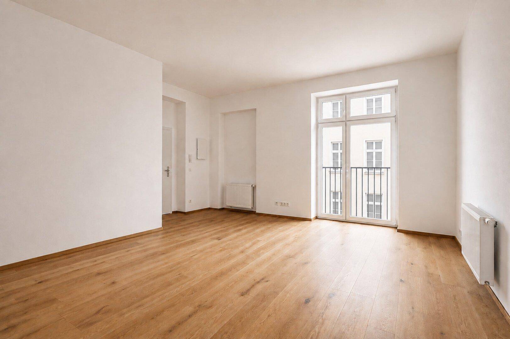 Geräumiges, unmöbliertes Wohnzimmer mit Holzboden und Zugang zu einem französischen Balkon.