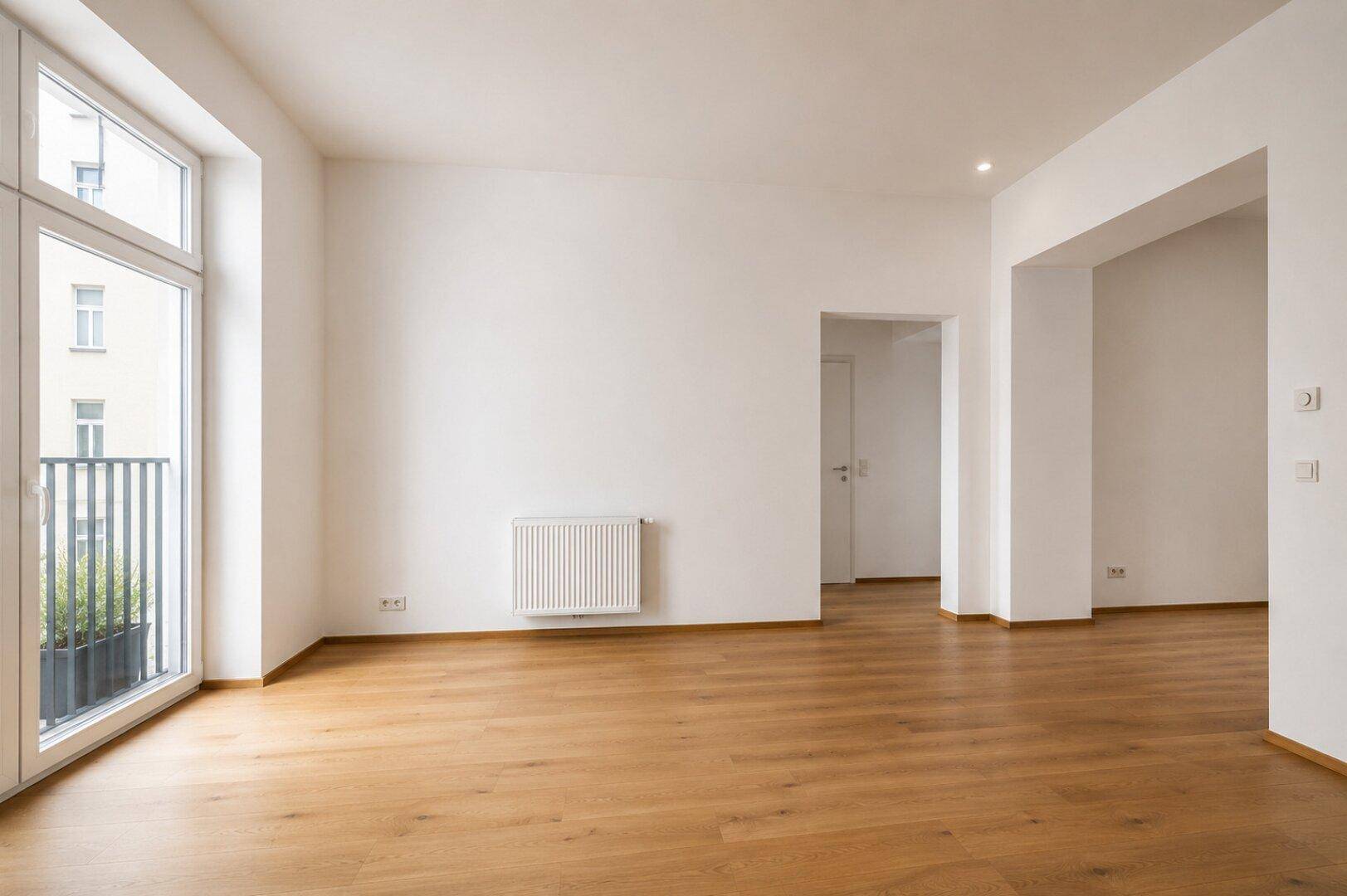 Heller, unmöblierter Raum mit Holzboden und großem Fenster, der als Wohnzimmer dienen könnte.