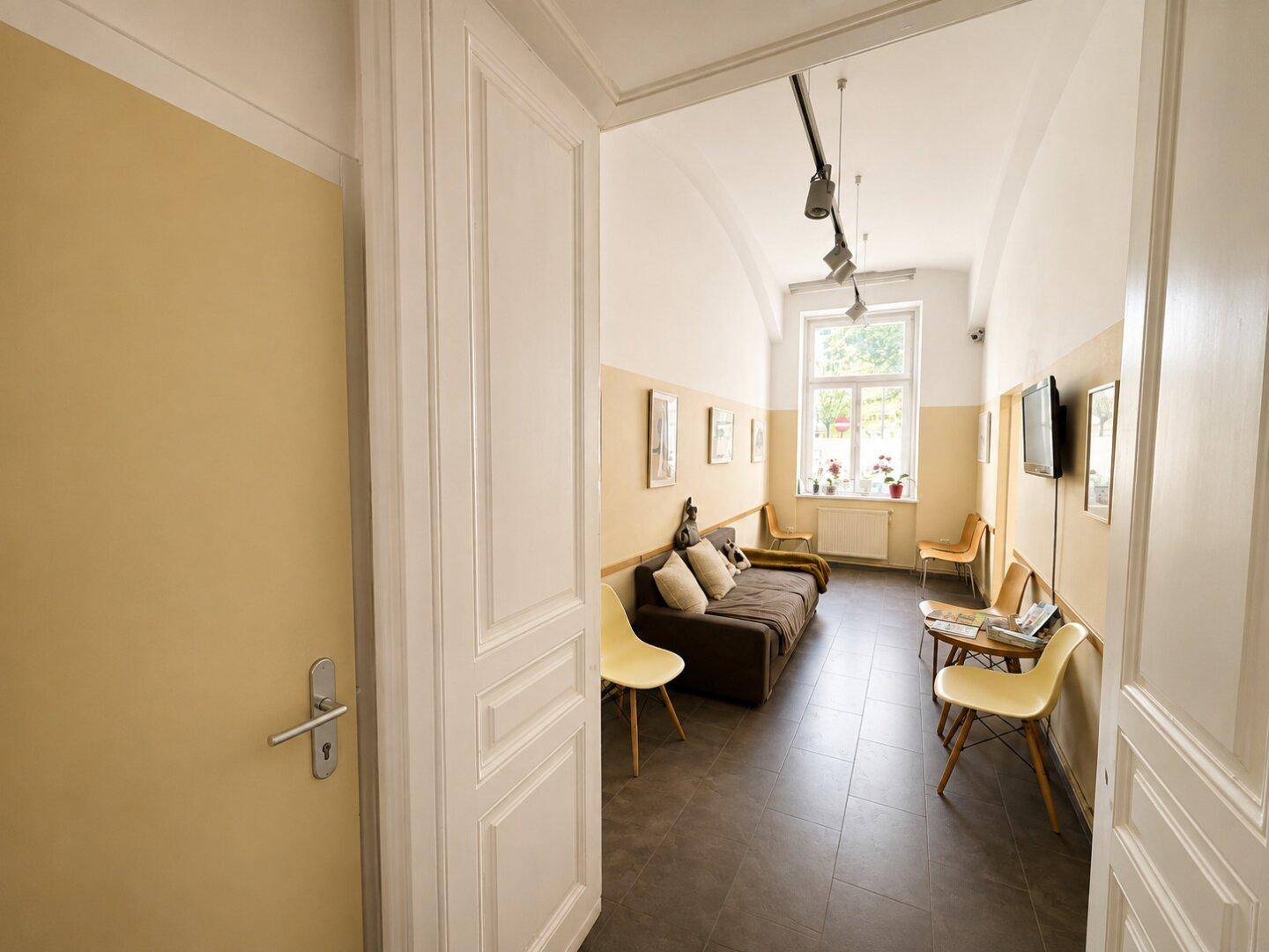 Blick in den hellen Flur mit Wartebereich, Fenstern und schlichten Möbeln.