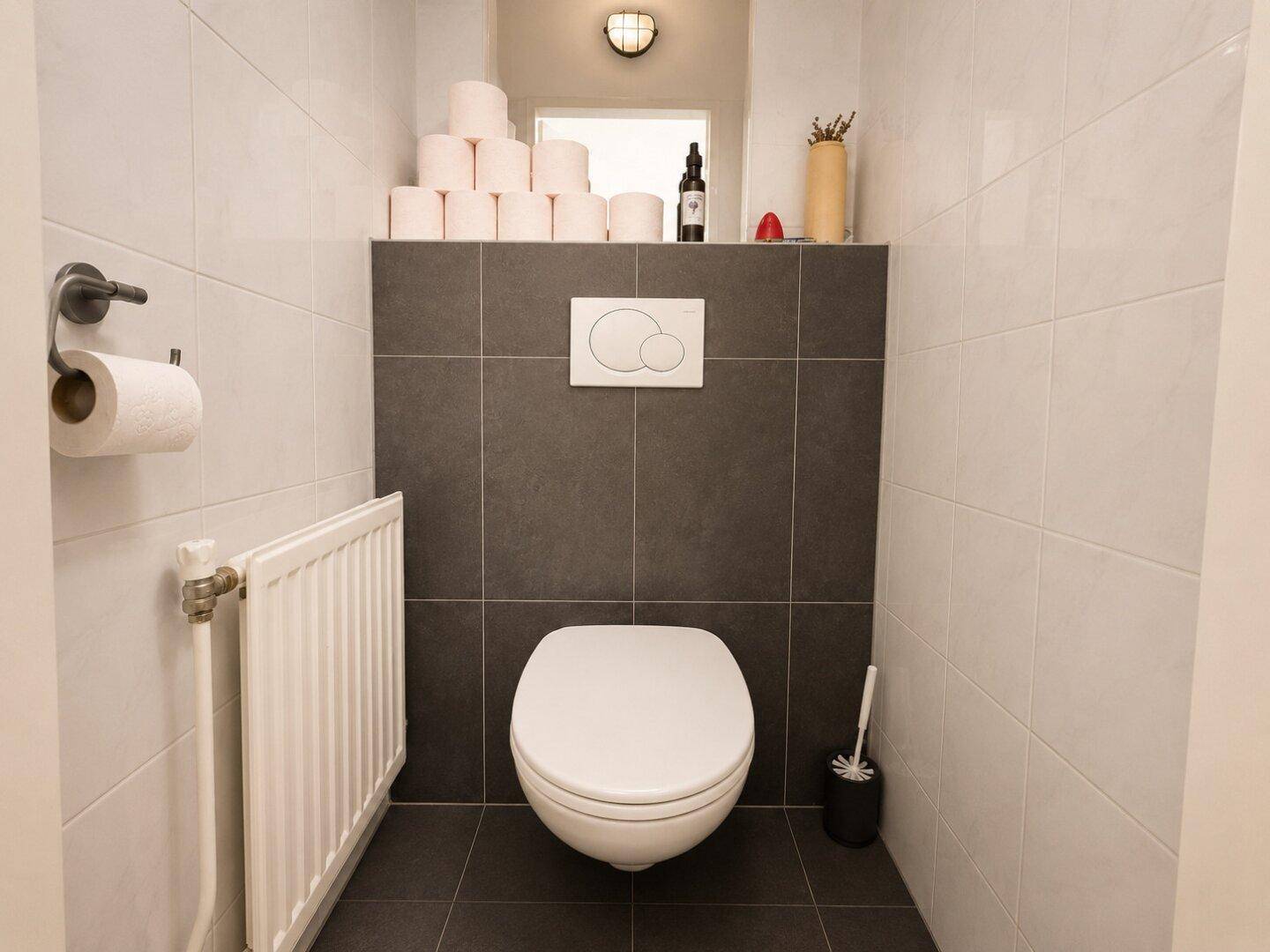 Modernes WC mit wandhängender Toilette, dunklen Fliesen und Heizkörper.