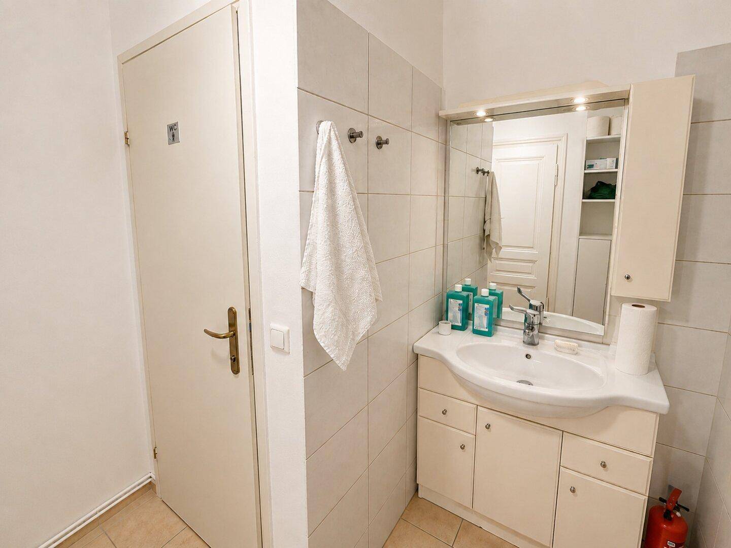 Badezimmer mit Waschbecken, Spiegelschrank und hellen Fliesen an den Wänden.
