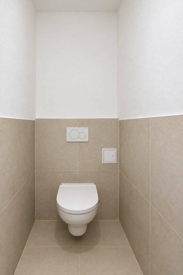 Modernes Gäste-WC mit wandhängender Toilette und beigefarbenen Fliesen, minimalistisch gestaltet.