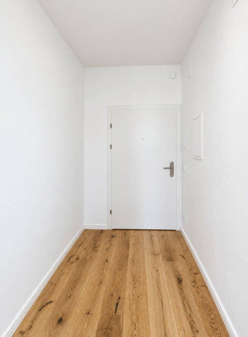 Heller, leerer Flur mit Holzboden und weiß gestrichenen Wänden, einladender Eingangsbereich.