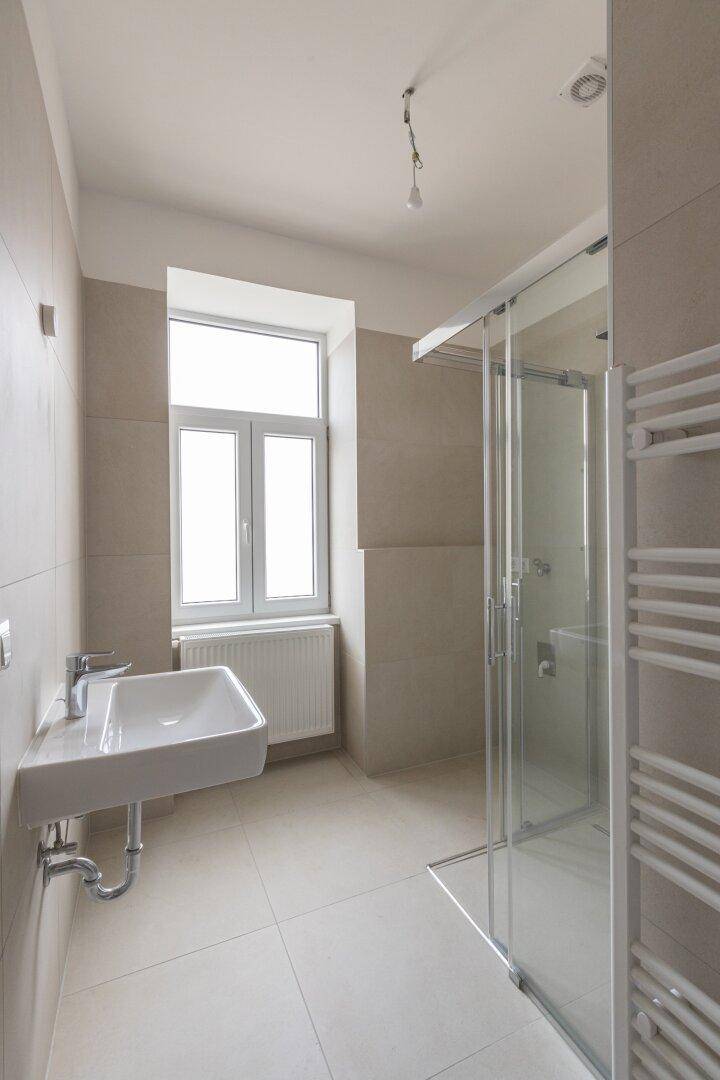 Modernes Badezimmer mit Fenster, Dusche und Einzelwaschbecken, hell und funktional.