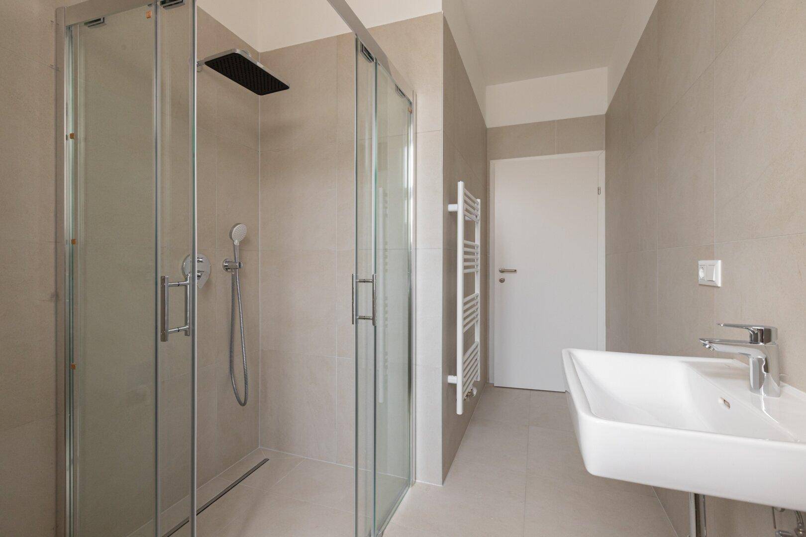 Helles Badezimmer mit moderner Dusche, Einzelwaschbecken und beheiztem Handtuchhalter.