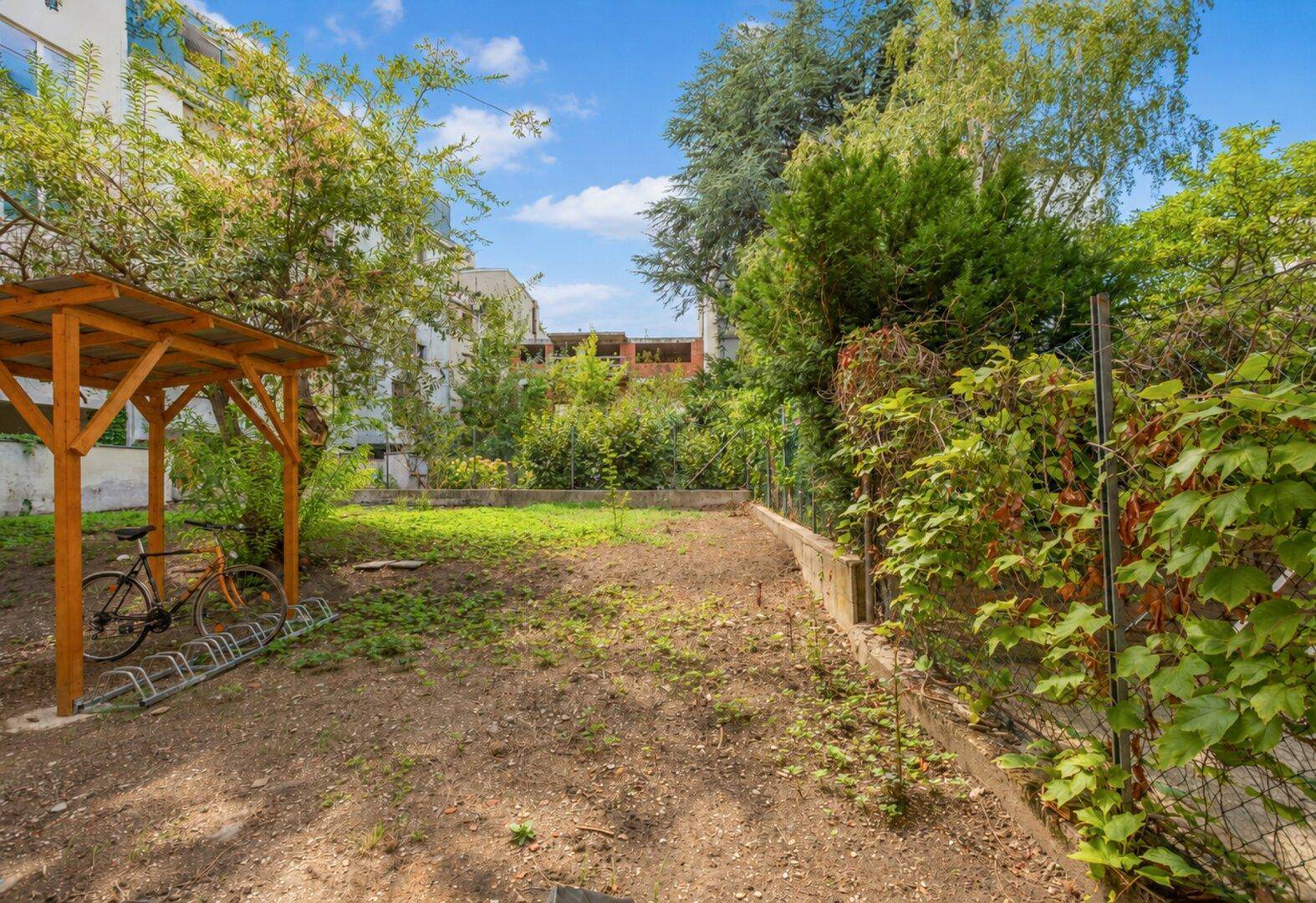 Ungepflegter Gartenbereich mit Fahrradunterstand und viel Grün, bereit zur Neugestaltung.