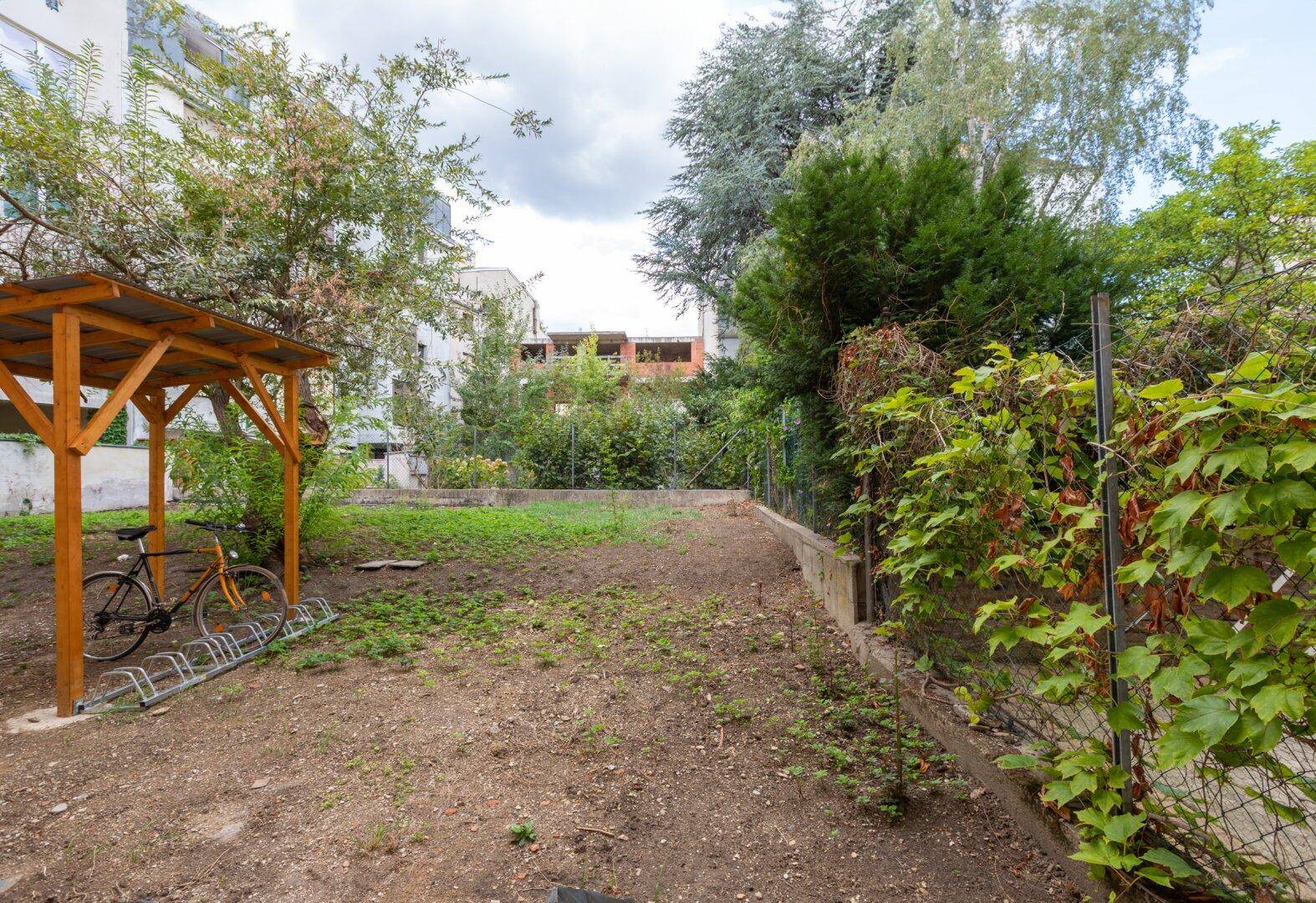 Ungepflegter Gartenbereich mit Fahrradunterstand und viel Grün, bereit zur Neugestaltung.