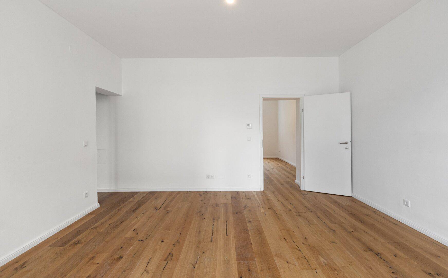 Geräumiges, unmöbliertes Zimmer mit Holzboden und weiß gestrichenen Wänden, vielseitig nutzbar.