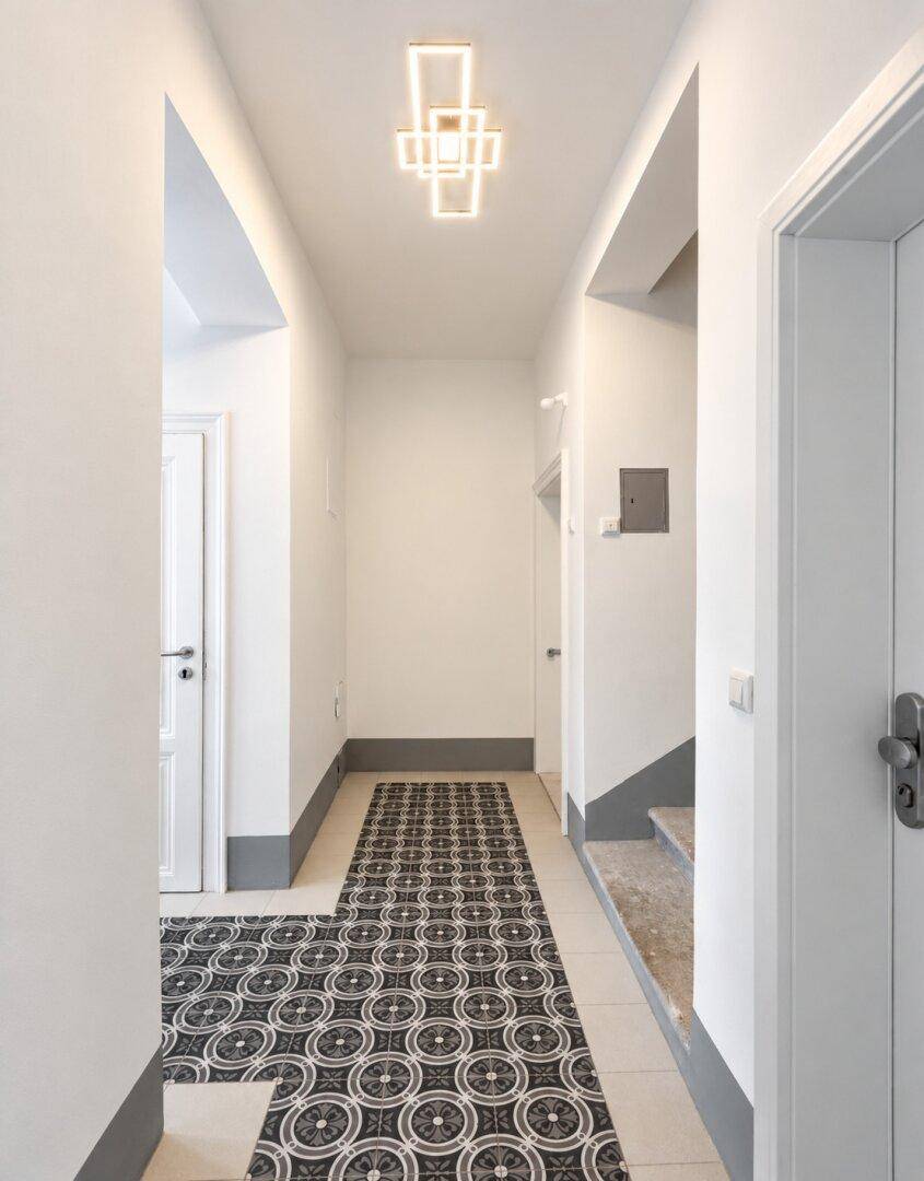 Heller Flur mit gemusterten Fliesen und moderner Deckenbeleuchtung, führt zum Treppenhaus.