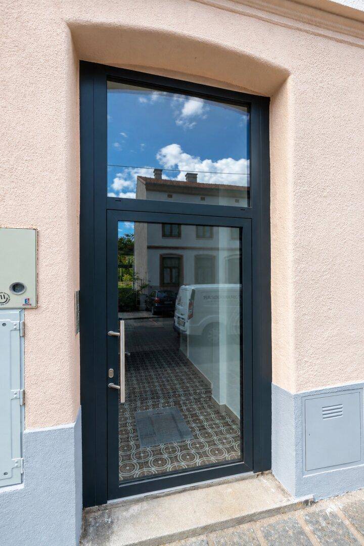 Moderner Hauseingang mit großer Glastür und reflektierendem Himmel, einladend und hell.