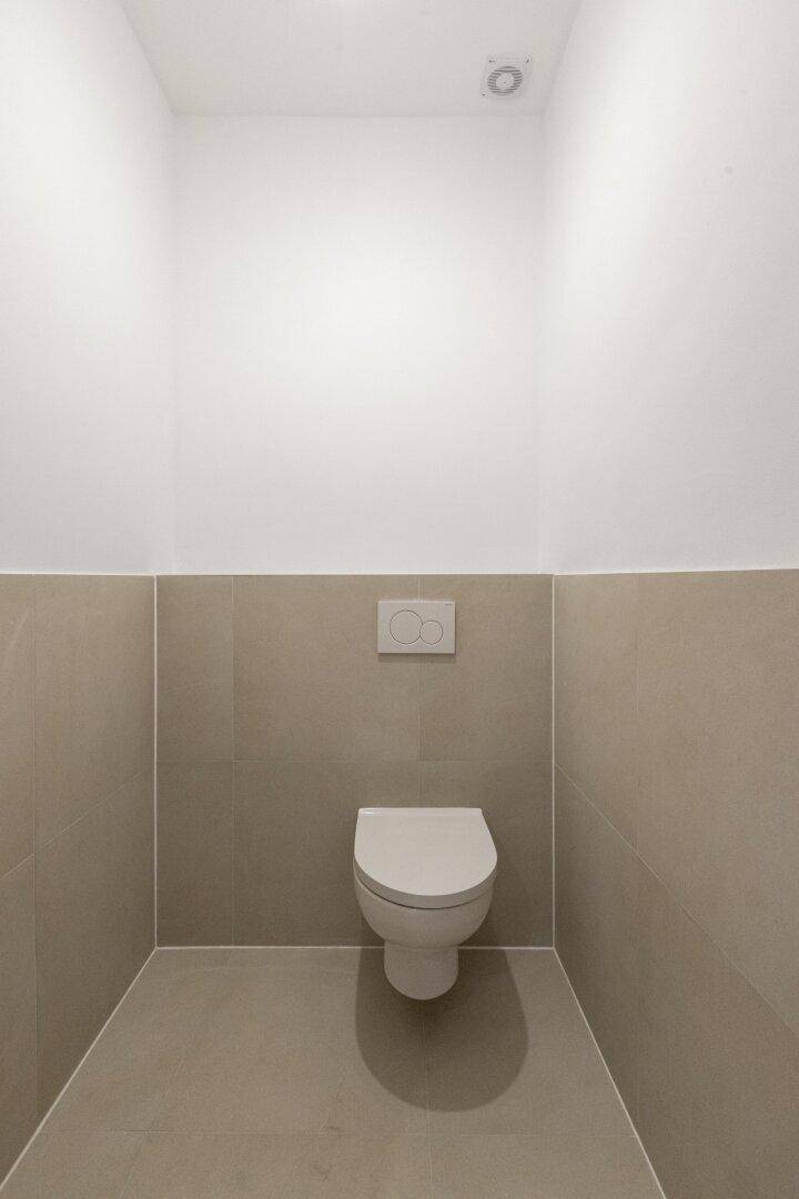 Separates WC mit Wand-WC und beigefarbenen Fliesen, sauber und funktional gestaltet.