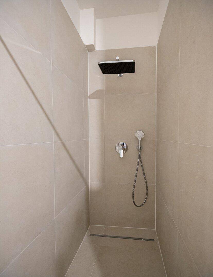 Begehbare Dusche mit Regenduschkopf und beigefarbenen Fliesen in modernem, minimalistischem Design.