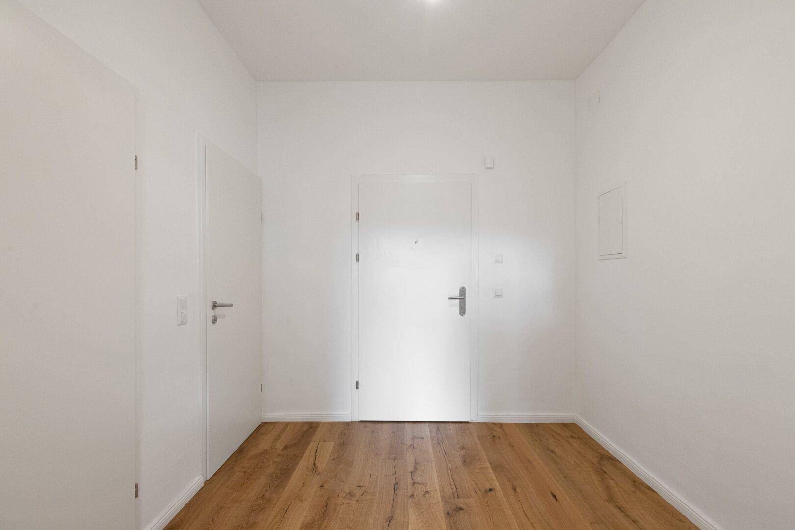 Heller Flur mit Holzboden und weißen Türen, der den Eingangsbereich der Wohnung erschließt.