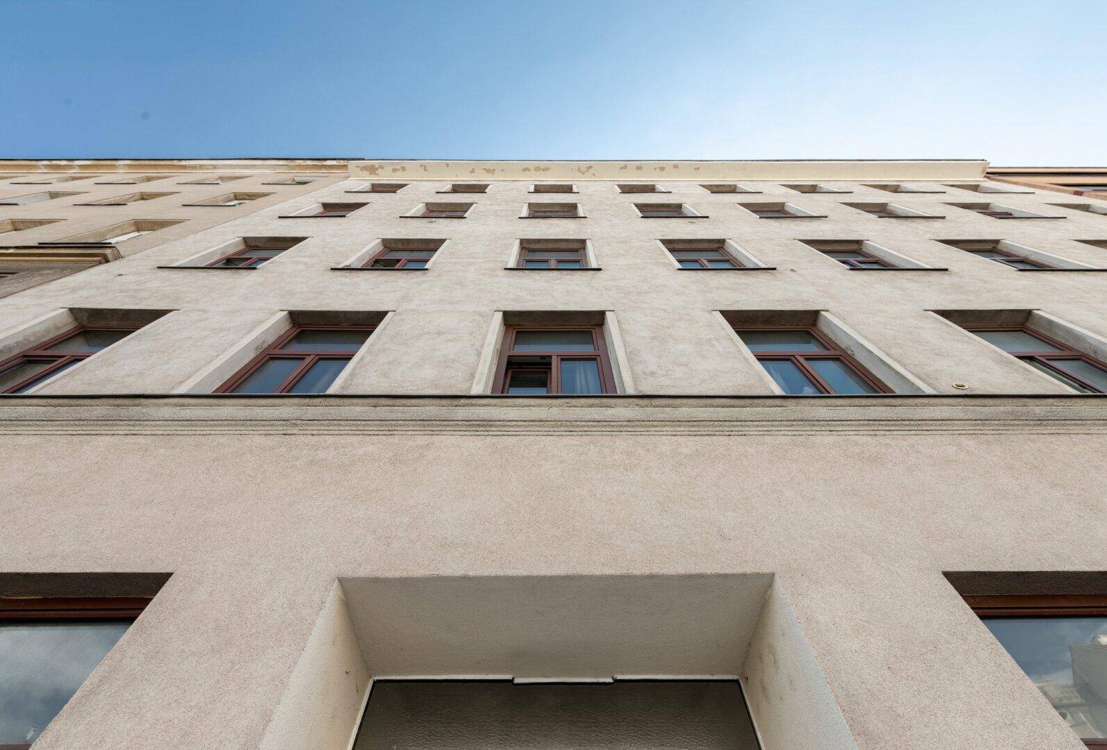 Fassade eines Altbaus mit vielen Fenstern und Putzstruktur, von unten fotografiert.