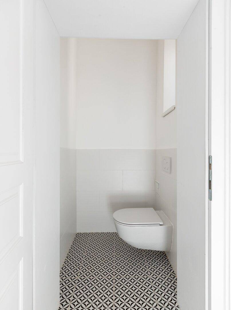 Kleines, modernes Gäste-WC mit wandhängender Toilette und gemustertem Fliesenboden.