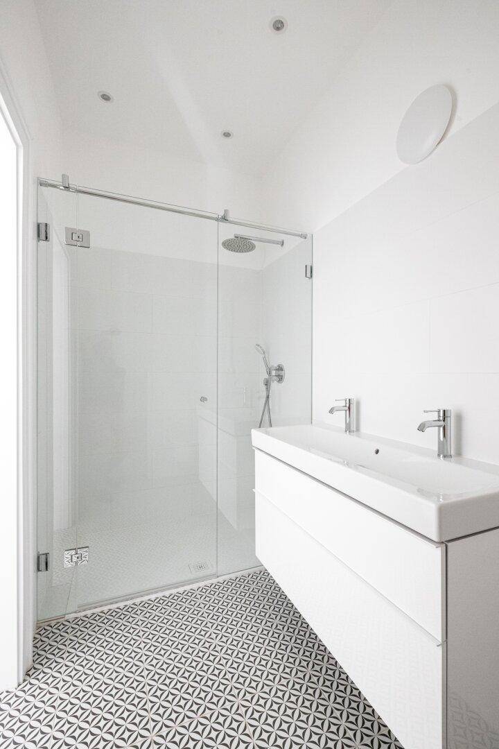 Modernes Badezimmer mit Doppelwaschbecken, großer Duschkabine und gemusterten Fliesen.