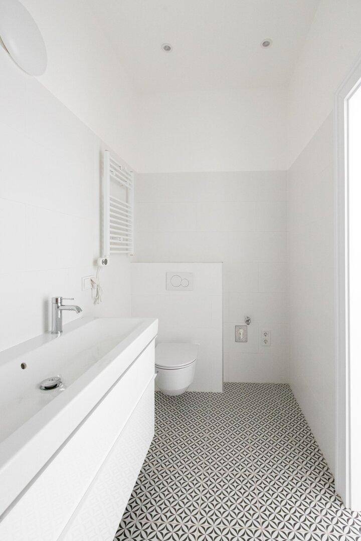 Helles Badezimmer mit wandhängendem WC, Einzelwaschbecken und beheiztem Handtuchhalter.