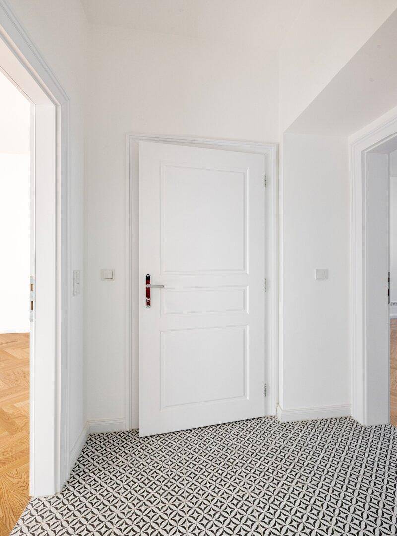 Heller Flur mit auffälligem schwarz-weißem Fliesenboden und weißer Tür.