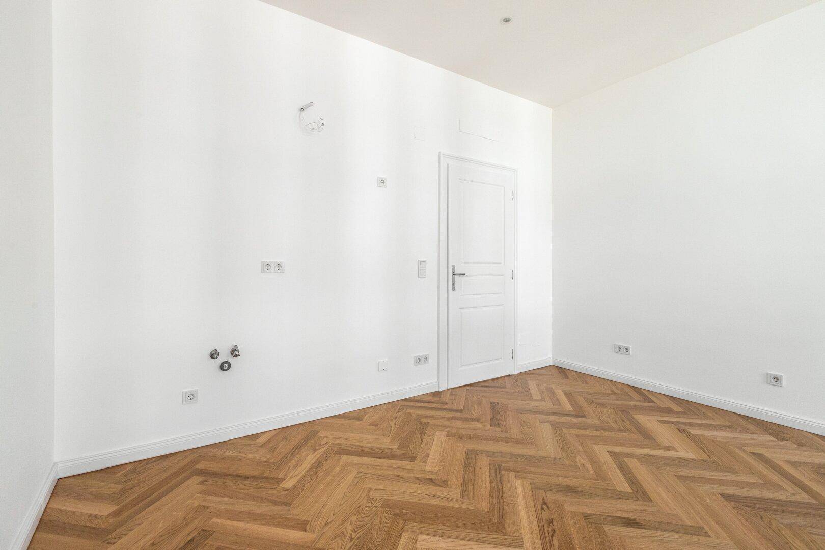 Heller Raum mit Fischgrätparkett, weißen Wänden und einer modernen Innentür.