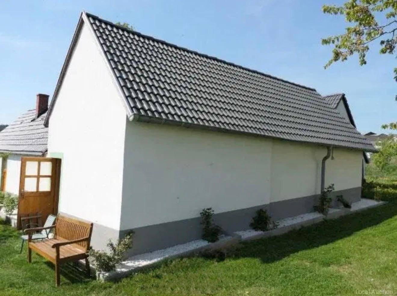 Seitenansicht des Hauses mit dunklem Ziegeldach, weißer Fassade und einer Holzbank im Gartenbereich.