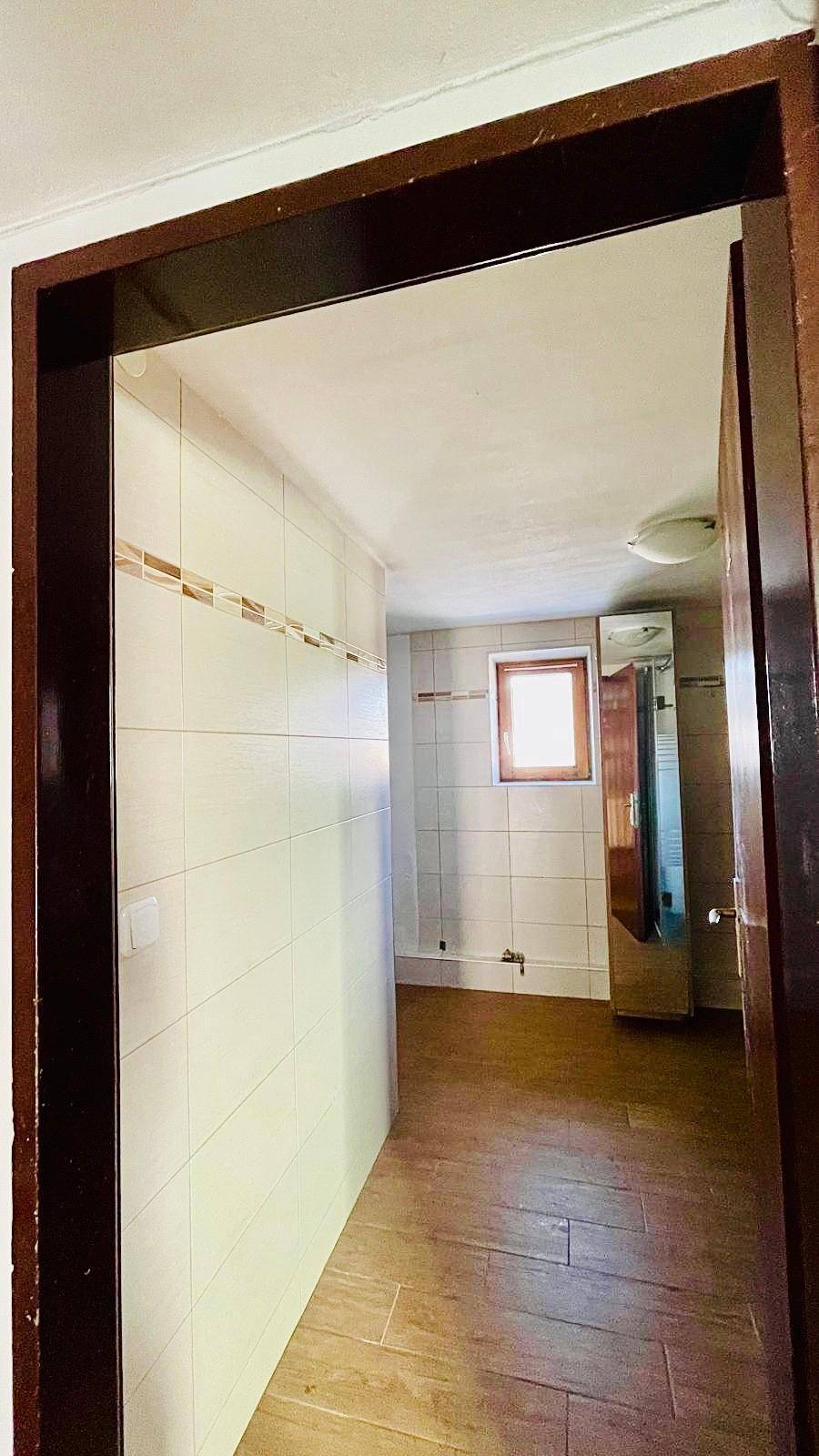 Gefliester Bereich, der zu einem Badezimmer oder WC führt, mit Fenster.