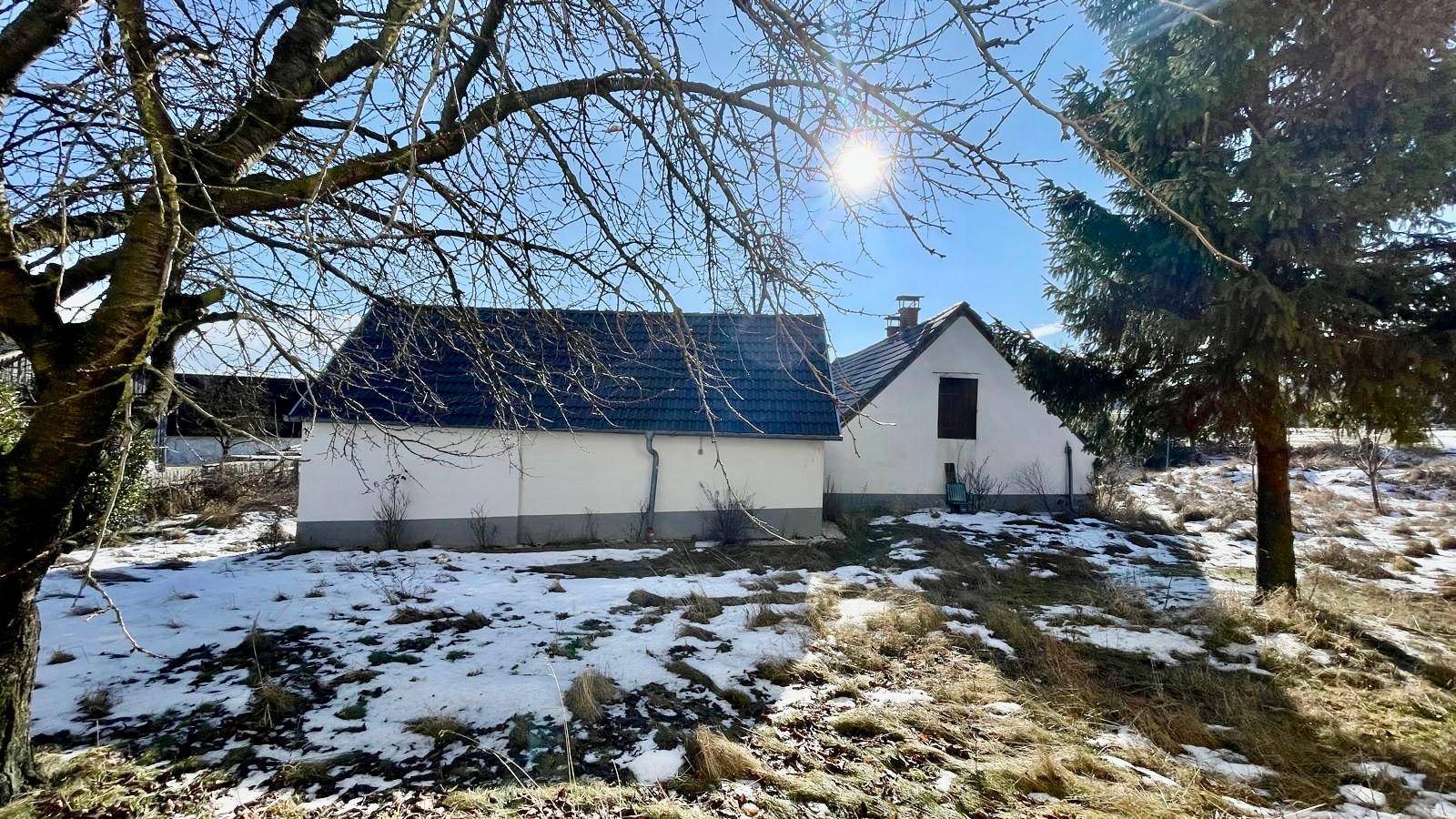 Ländliches Haus mit Satteldach und verschneiter Umgebung unter blauem Himmel.