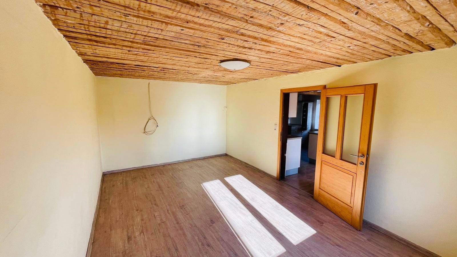 Heller Raum mit Holzbalkendecke und Laminatboden, ideal als Wohnbereich.