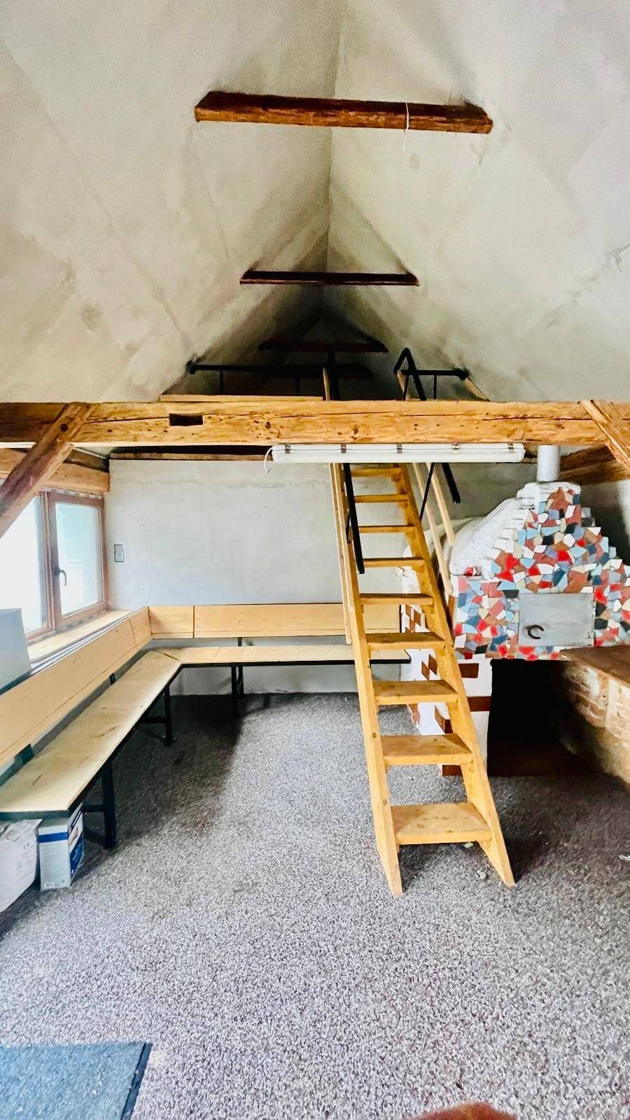 Geräumiger Dachboden mit Holzleiter, Sitzgelegenheiten und rustikalem Ofen.