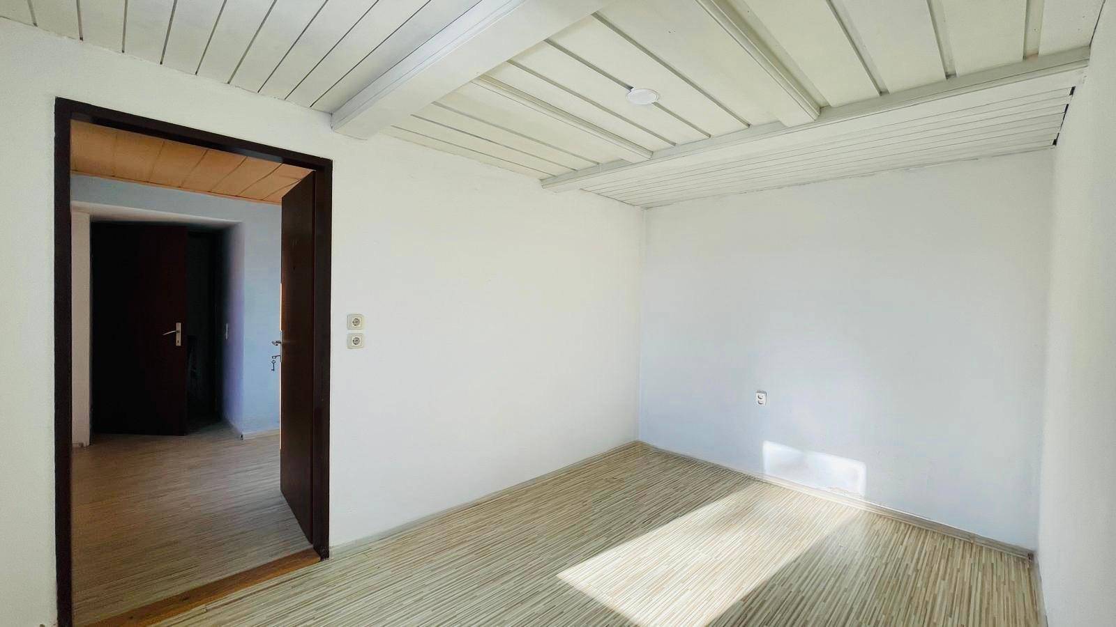 Helles Schlafzimmer mit weiß gestrichenen Holzbalken und Laminatboden.