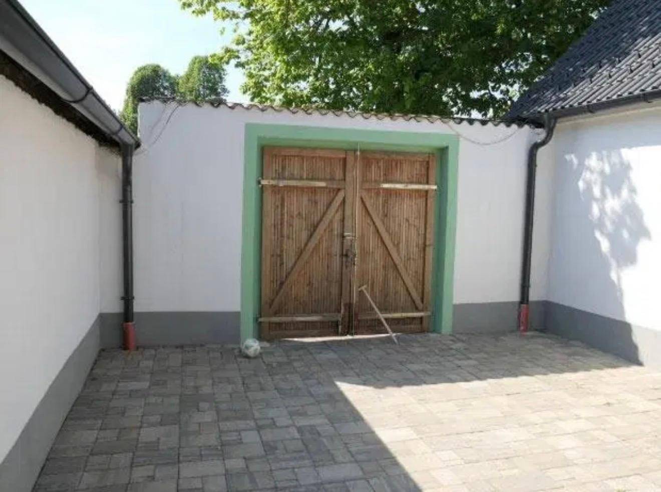 Gepflasterter Innenhof mit großen Holztoren, umgeben von weißen Wänden und grünem Rahmen.