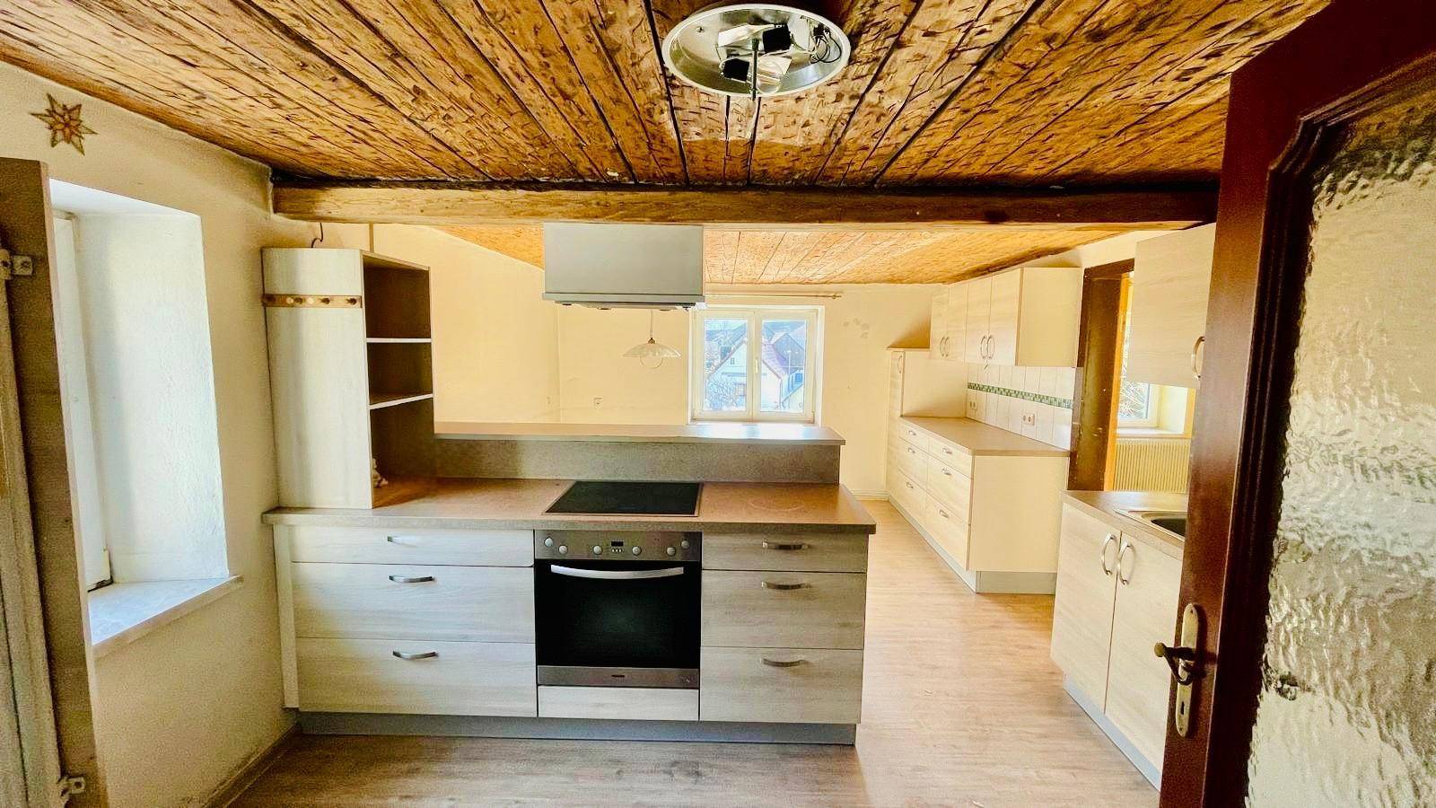Helle Küche mit Holzbalkendecke, Einbaugeräten und Blick nach draußen.