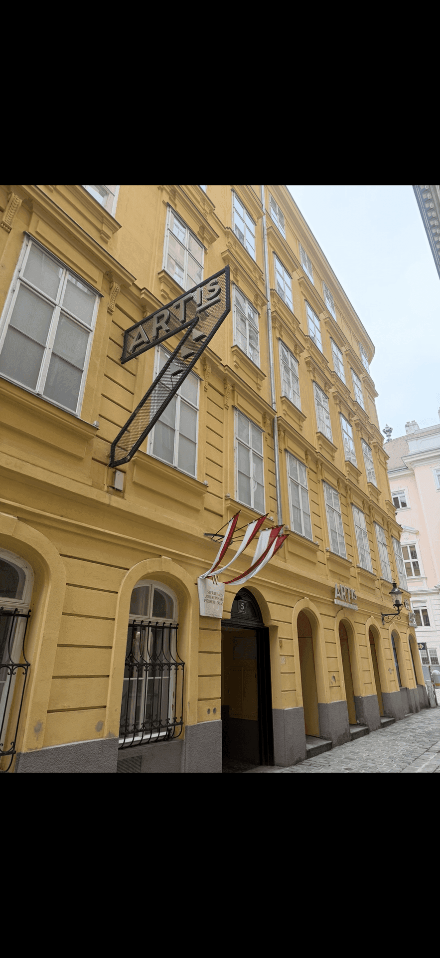 Detailansicht der gelben Fassade eines historischen Gebäudes mit Eingang und Werbeschild.