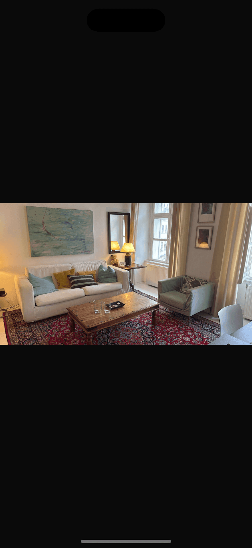 Gemütliches Wohnzimmer mit weißem Sofa, Teppich und Blick auf die Stadt durch das Fenster.