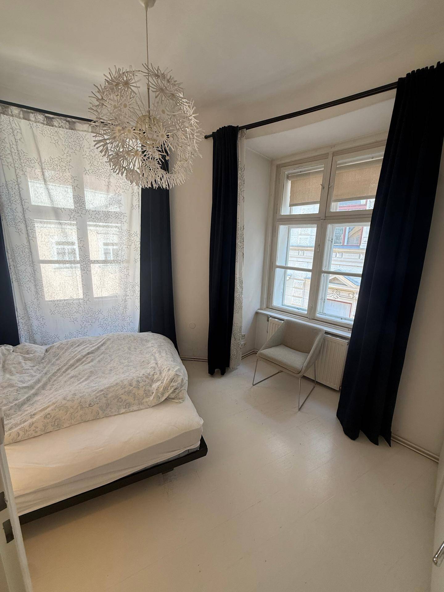 Geräumiges Schlafzimmer mit großen Fenstern, die viel Tageslicht hereinlassen, und einem Sessel.