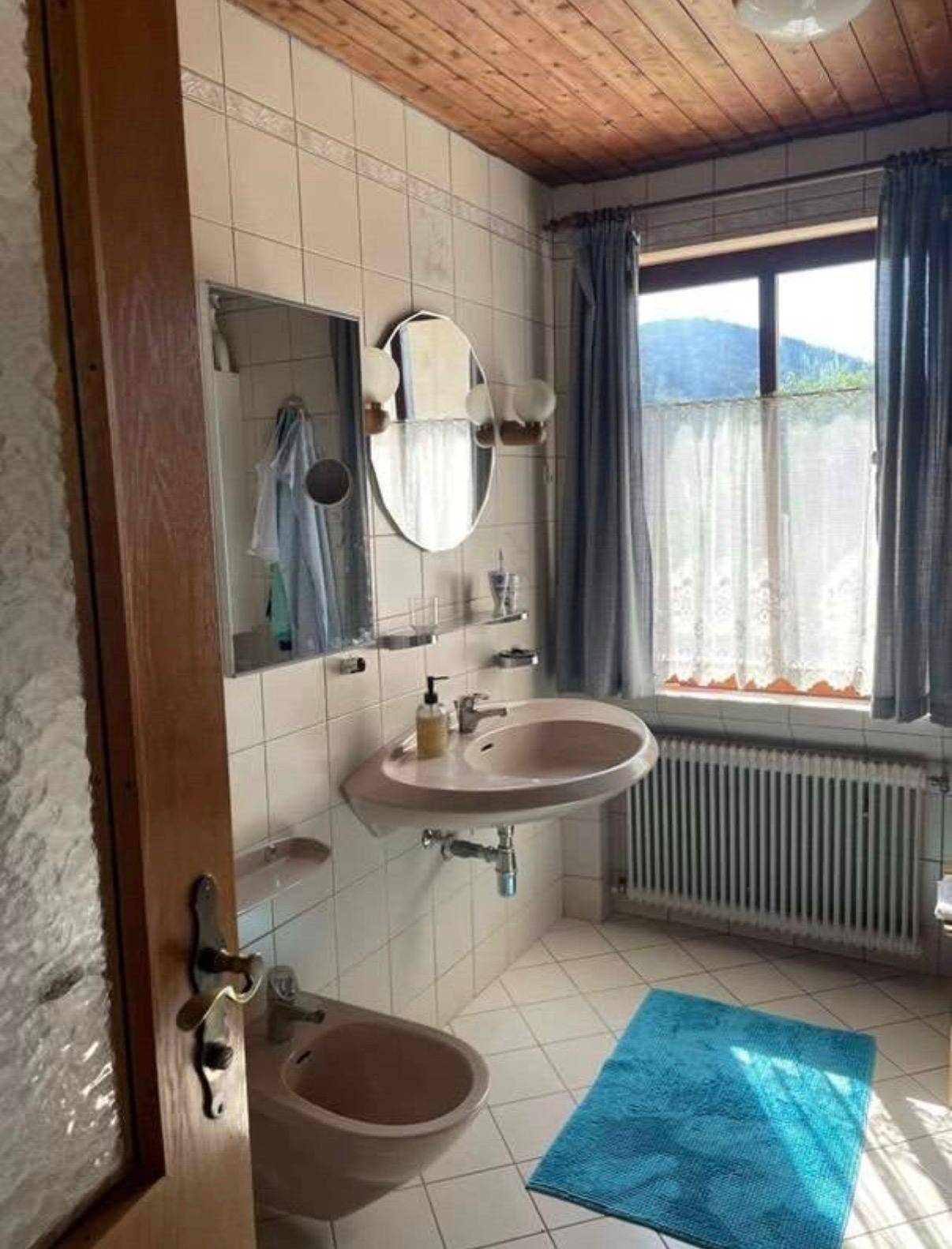 Helles Badezimmer mit beigen Fliesen, Einzelwaschbecken, Bidet und Fenster mit Bergblick.