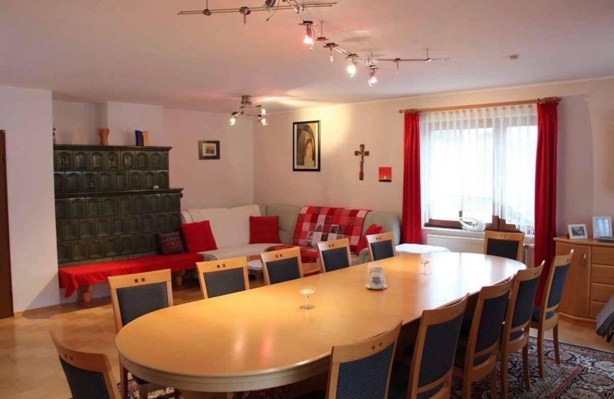 Geräumiger Wohn-Essbereich mit großem Holztisch, bequemer Sitzecke und einem traditionellen Kachelofen.