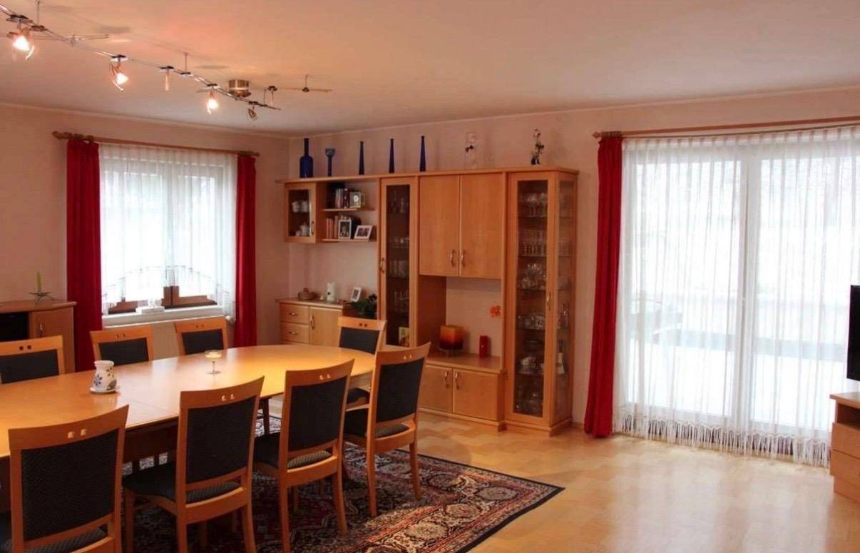 Heller Wohn-Essbereich mit Holzschränken, großem Fenster und Zugang zu einem möglichen Außenbereich.