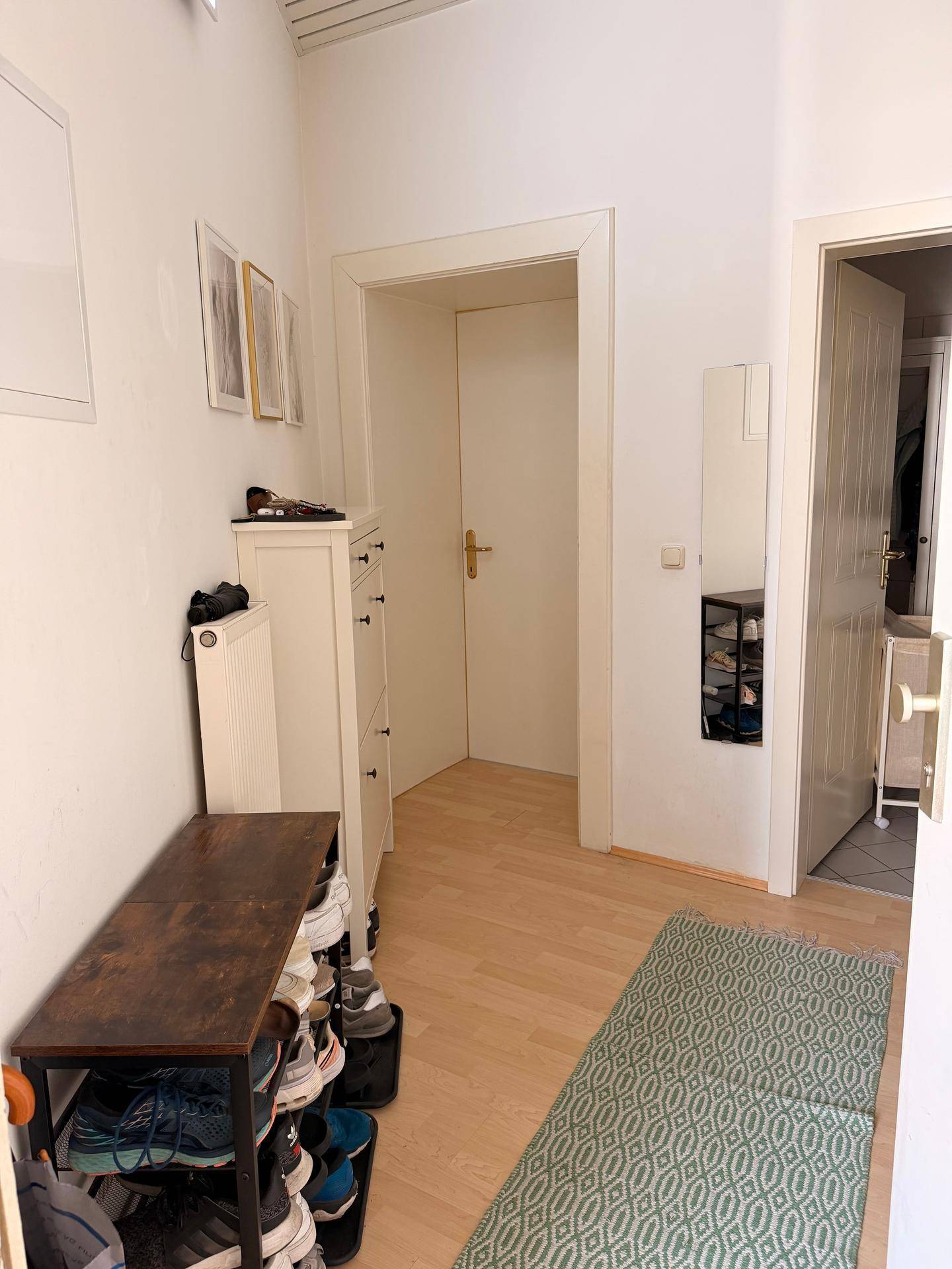 Schmaler Flur mit Schuhregalen, Spiegel und hellem Holzfußboden.
