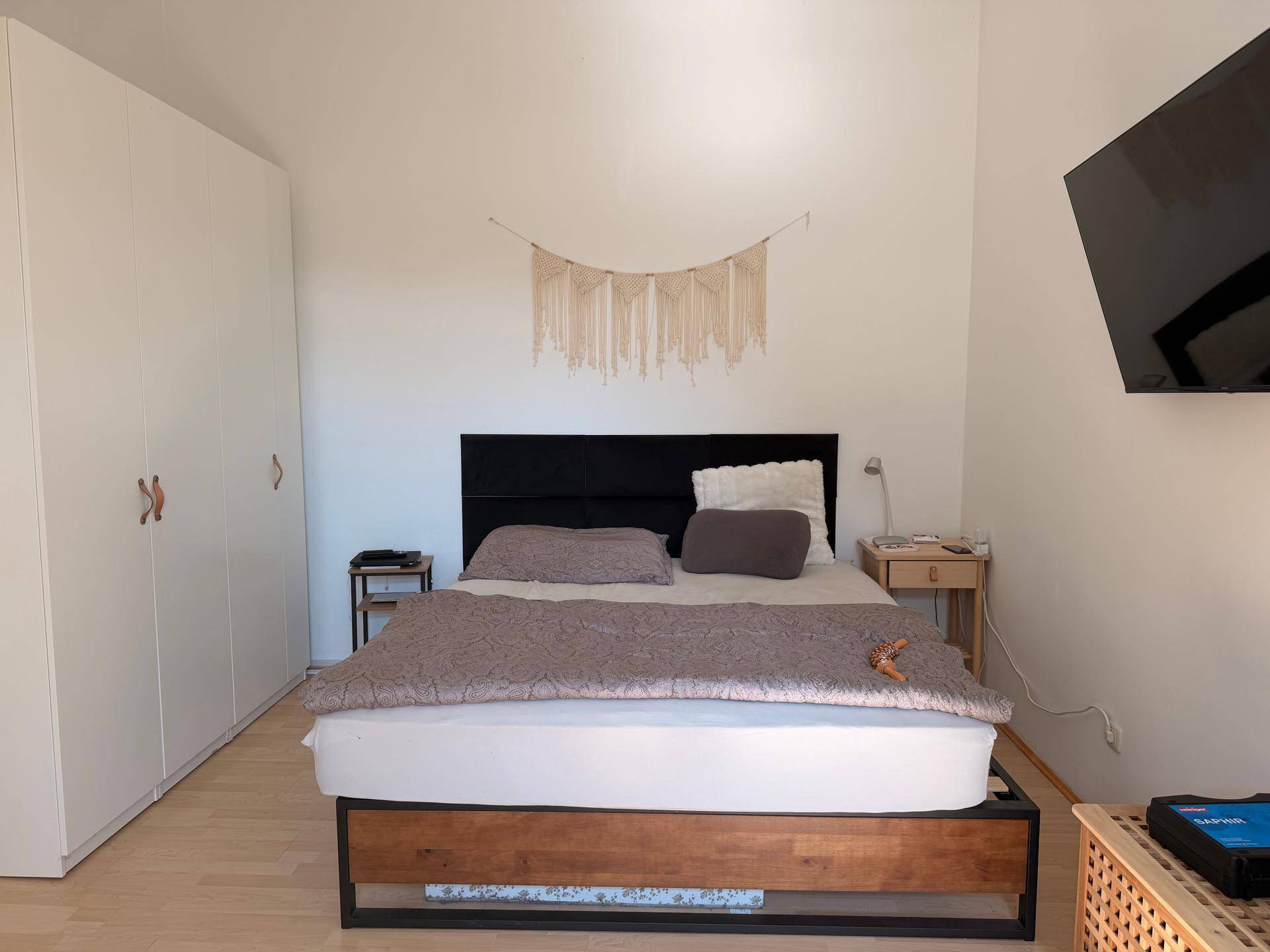 Schlafzimmer mit Doppelbett, großem weißen Kleiderschrank und Wandfernseher.